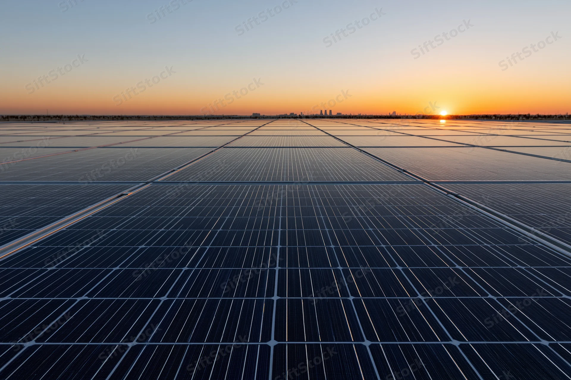 Large solar panel array stretching to the horizon at sunset with city skyline in distance