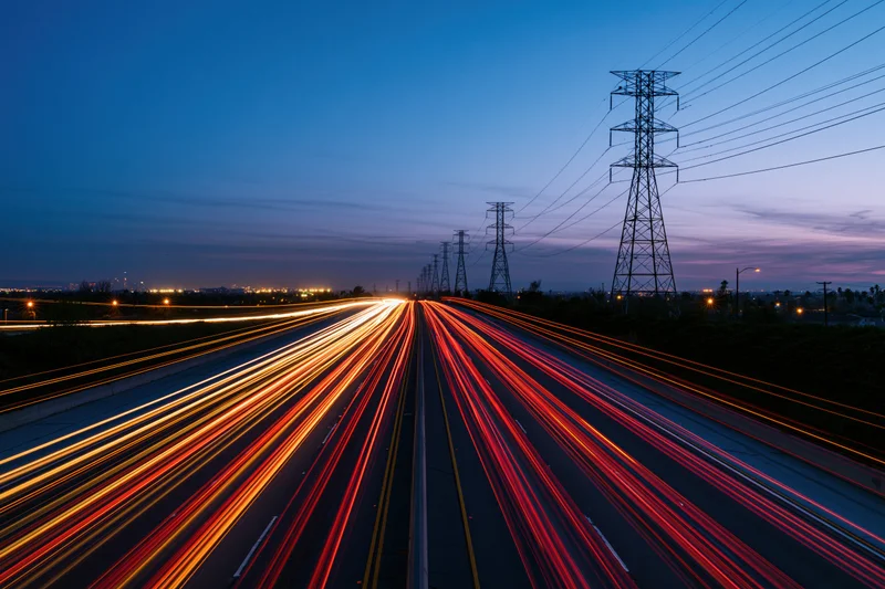 Long-exposure view of highway traffic with light trails at dusk under powerlines