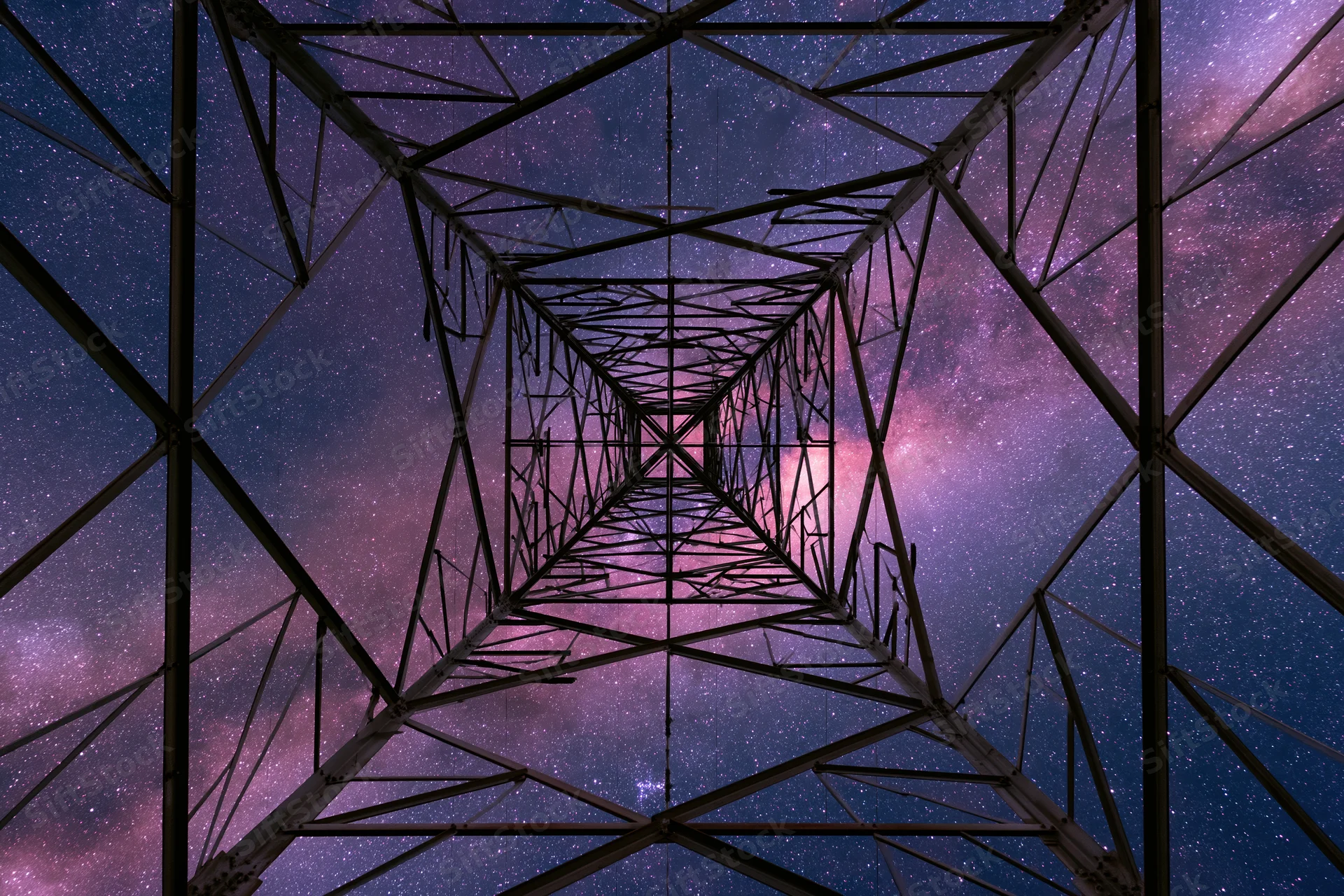Steel electricity transmission tower viewed from base looking up into starry night sky with milky way visible through lattice structure