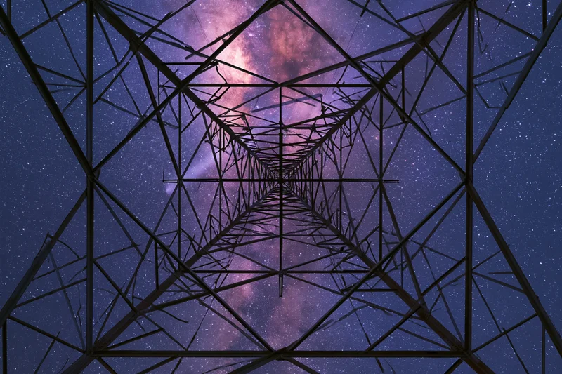 Steel electricity transmission tower viewed from base looking up at starry night sky with milky way visible through lattice structure