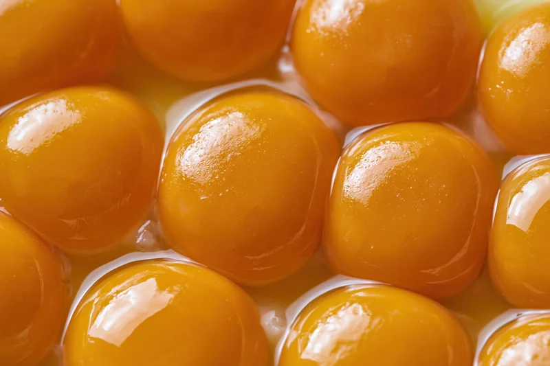 Multiple raw egg yolks closely packed in a bowl, glistening with liquid surrounding them