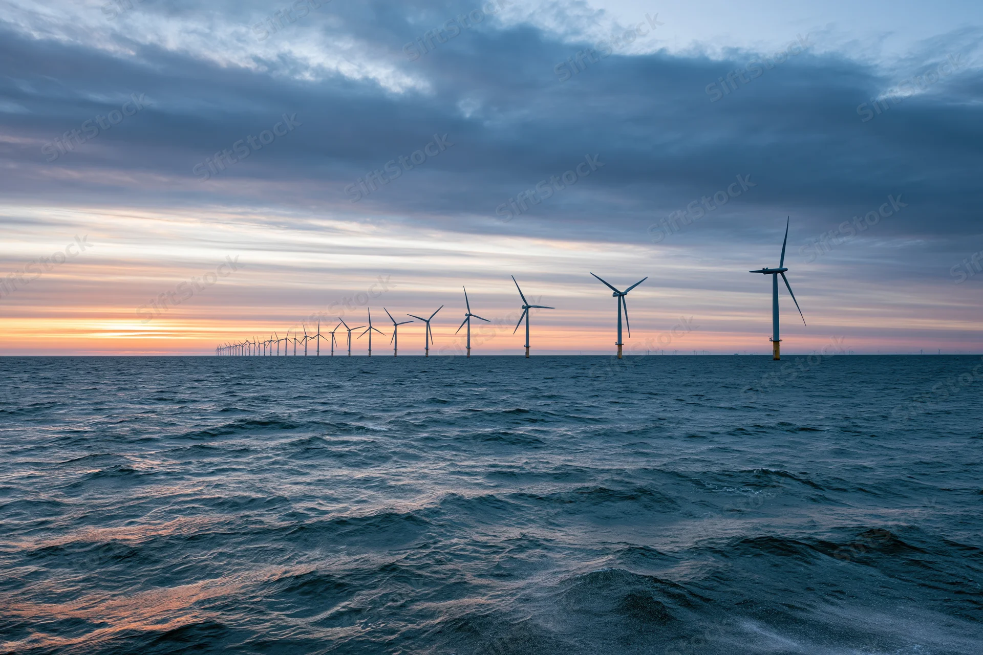 Offshore wind turbines stretching into the horizon over the ocean at sunset