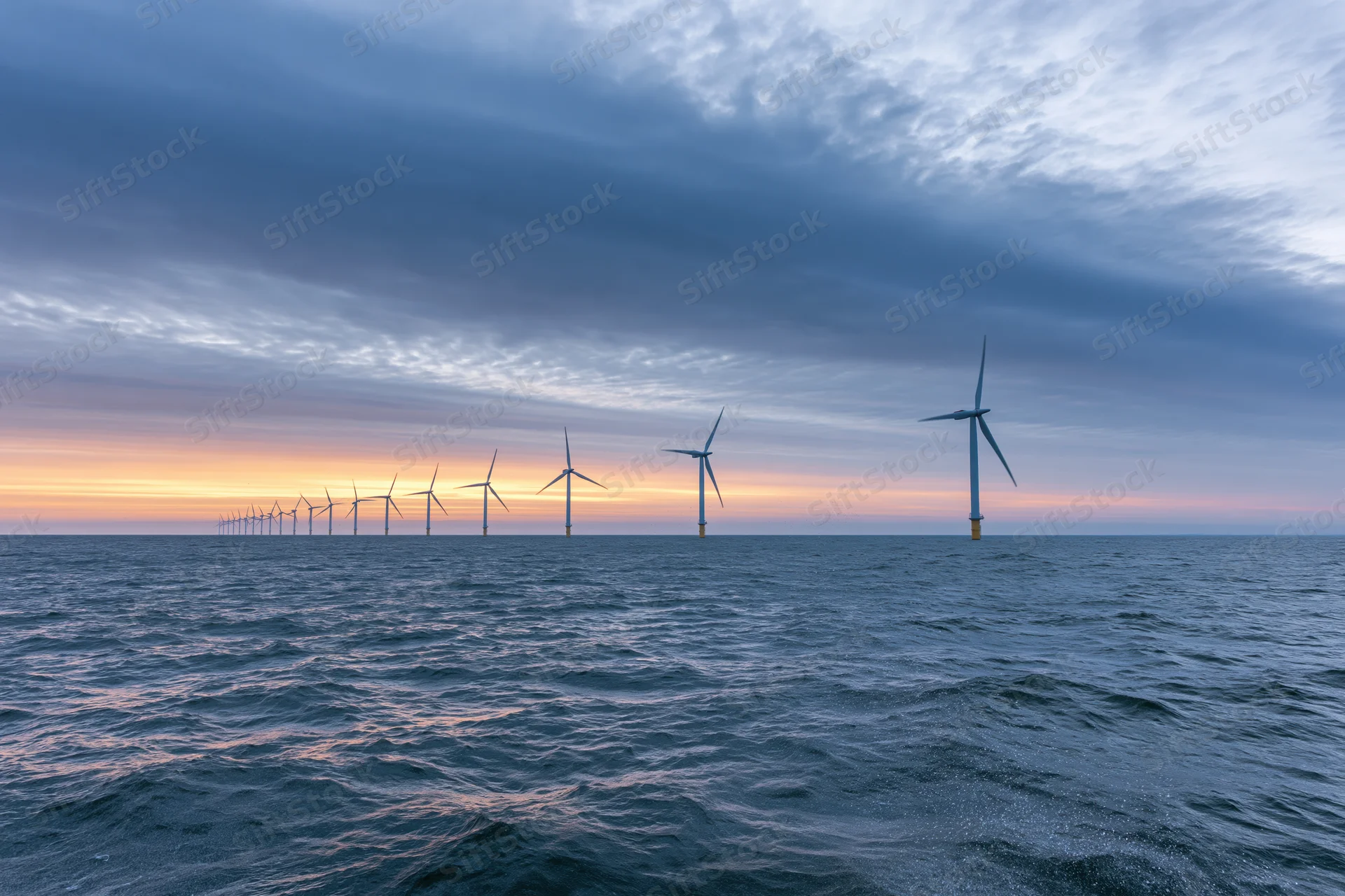 Offshore wind turbines stretching into the horizon over the ocean at sunset