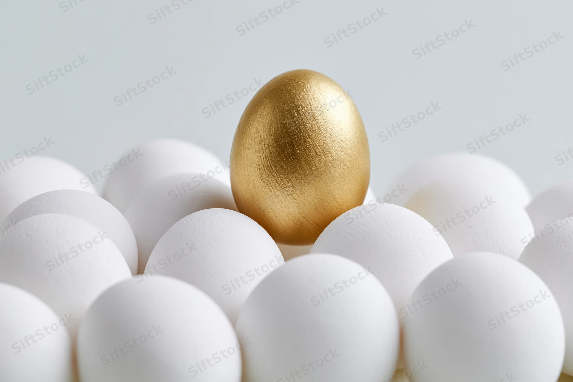 Golden egg standing among white eggs in a cluster on a plain surface