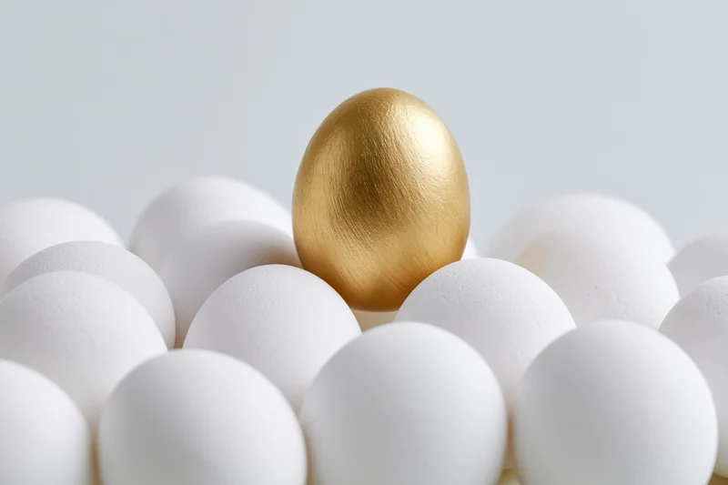 Golden egg standing among white eggs in a cluster on a plain surface