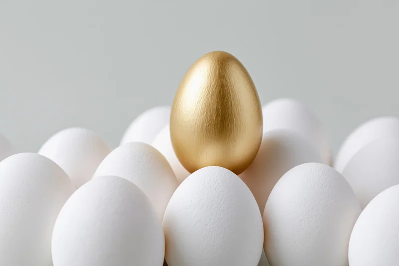 Golden egg standing among white eggs in a cluster, centered and elevated