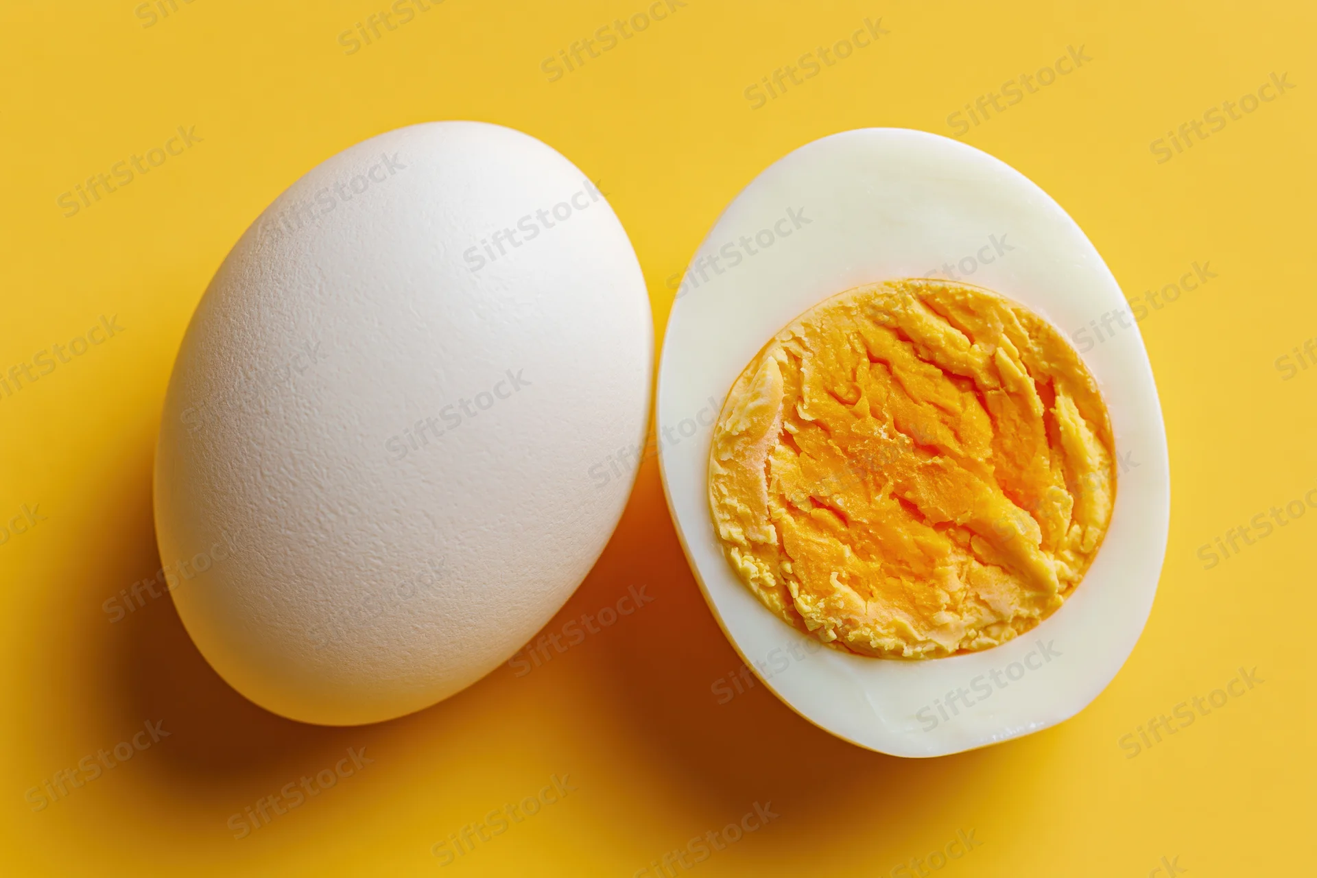 Whole white chicken egg beside halved hard-boiled egg on yellow background