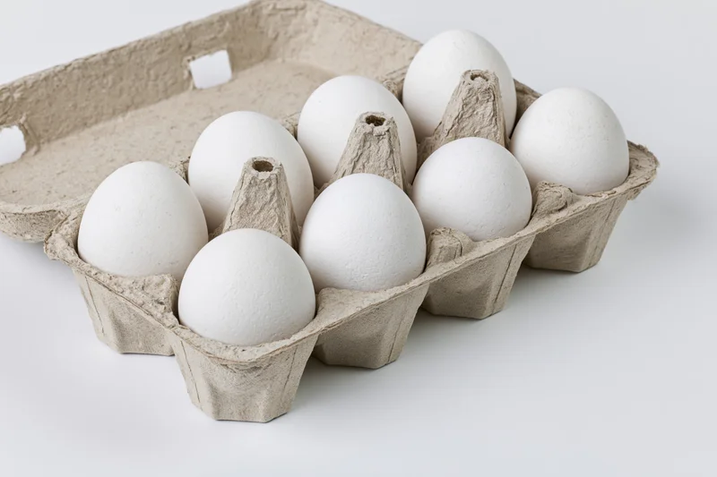 Open cardboard egg carton holding ten white eggs viewed from above on white background