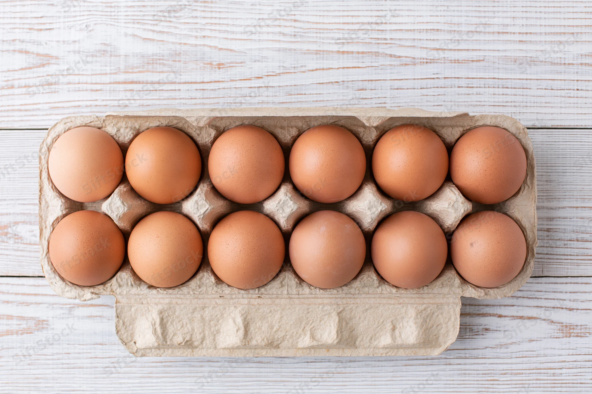 Twelve brown eggs arranged in an open cardboard carton on a wooden surface