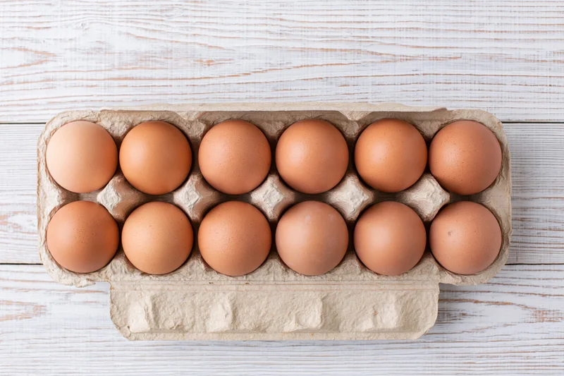 Twelve brown eggs arranged in an open cardboard carton on a wooden surface