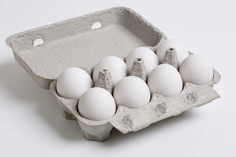 Open gray recycled cardboard egg carton holding ten white eggs on white background