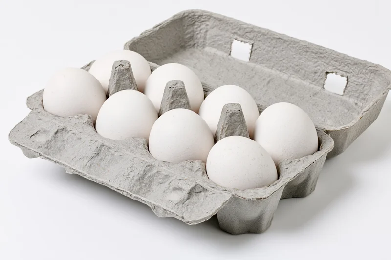 Open gray recycled cardboard egg carton holding ten white eggs on white background