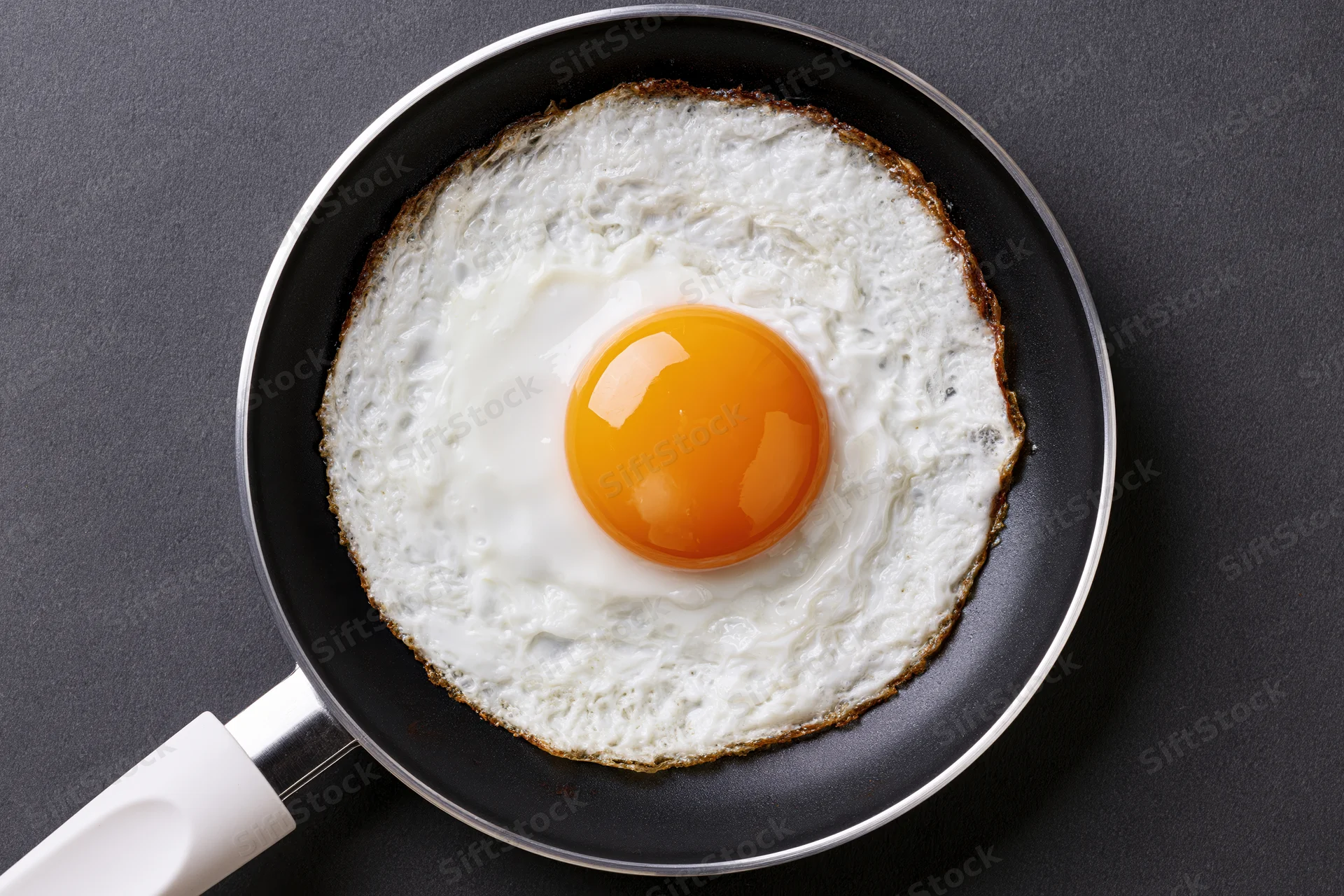 Single fried egg in a small black nonstick skillet viewed from above on a dark surface
