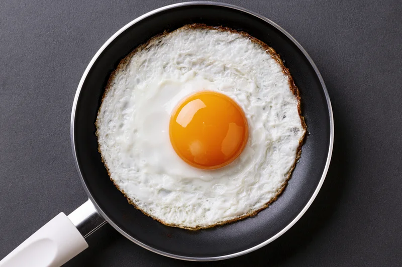 Single fried egg in a small black nonstick skillet viewed from above on a dark surface
