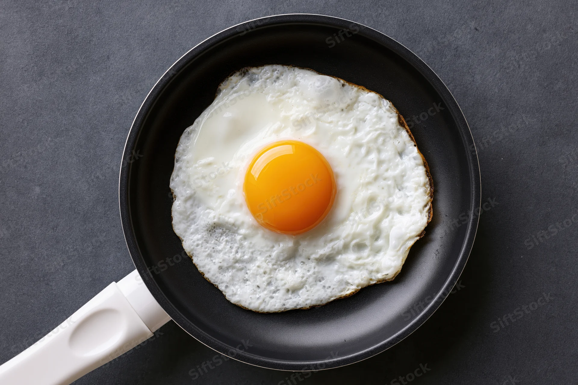 Single fried egg in a small black nonstick pan viewed from above on dark surface