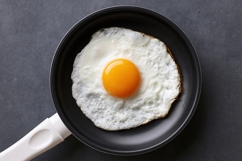 Single fried egg in a small black nonstick pan viewed from above on dark surface