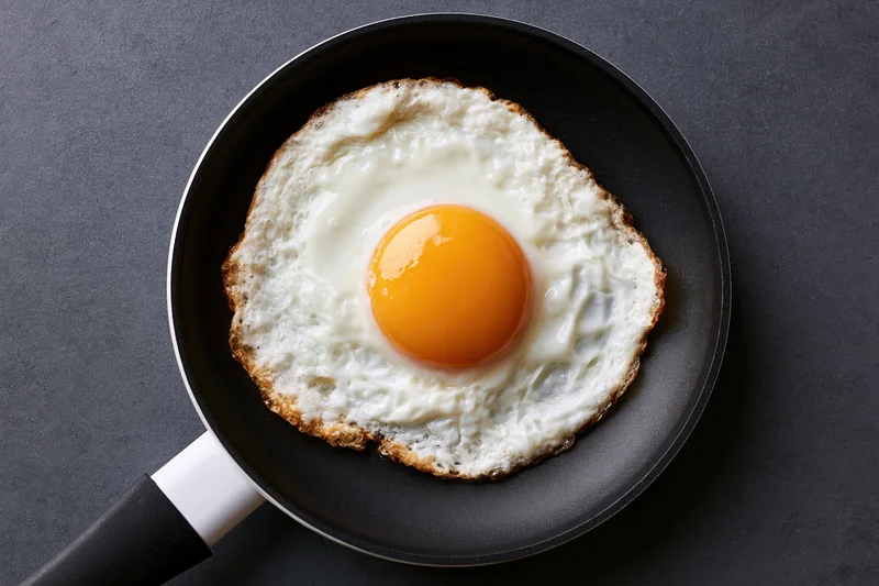 Single fried egg in a small black nonstick pan viewed from above on dark surface