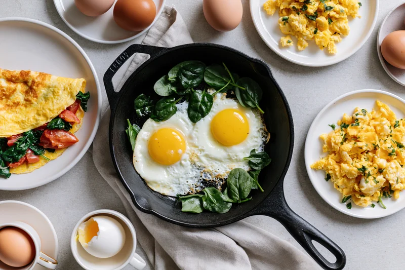 Multiple egg dishes arranged in a flat lay on a light surface with cast iron skillet and plates