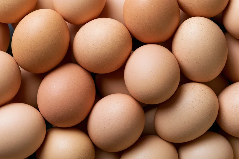 Pile of brown chicken eggs arranged closely in top-down view filling the frame