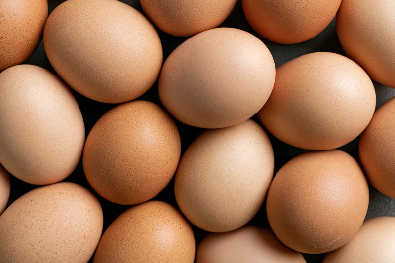 Pile of brown chicken eggs arranged closely in top-down view on dark surface