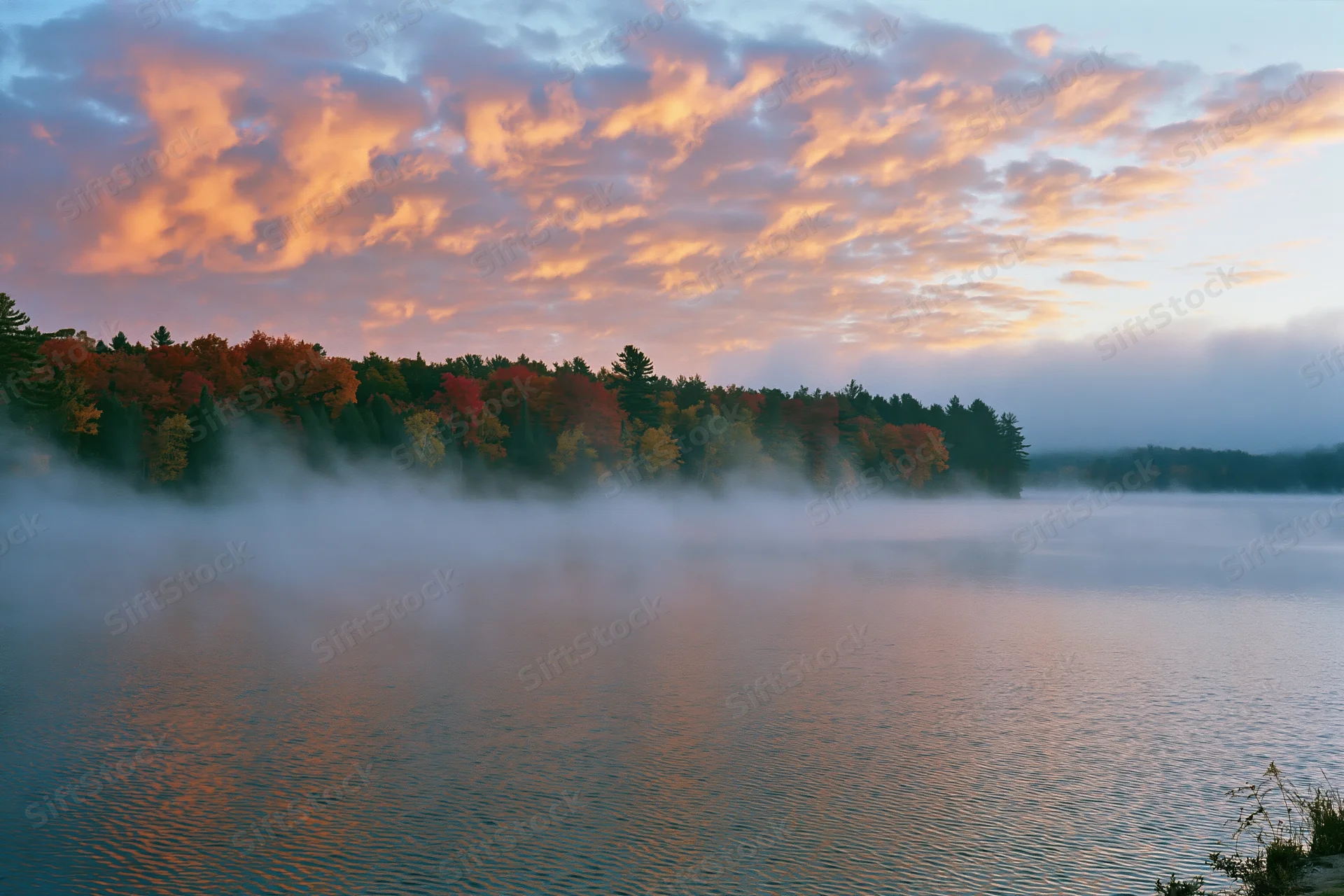 Misty lake reflecting autumn trees at early morning sunrise