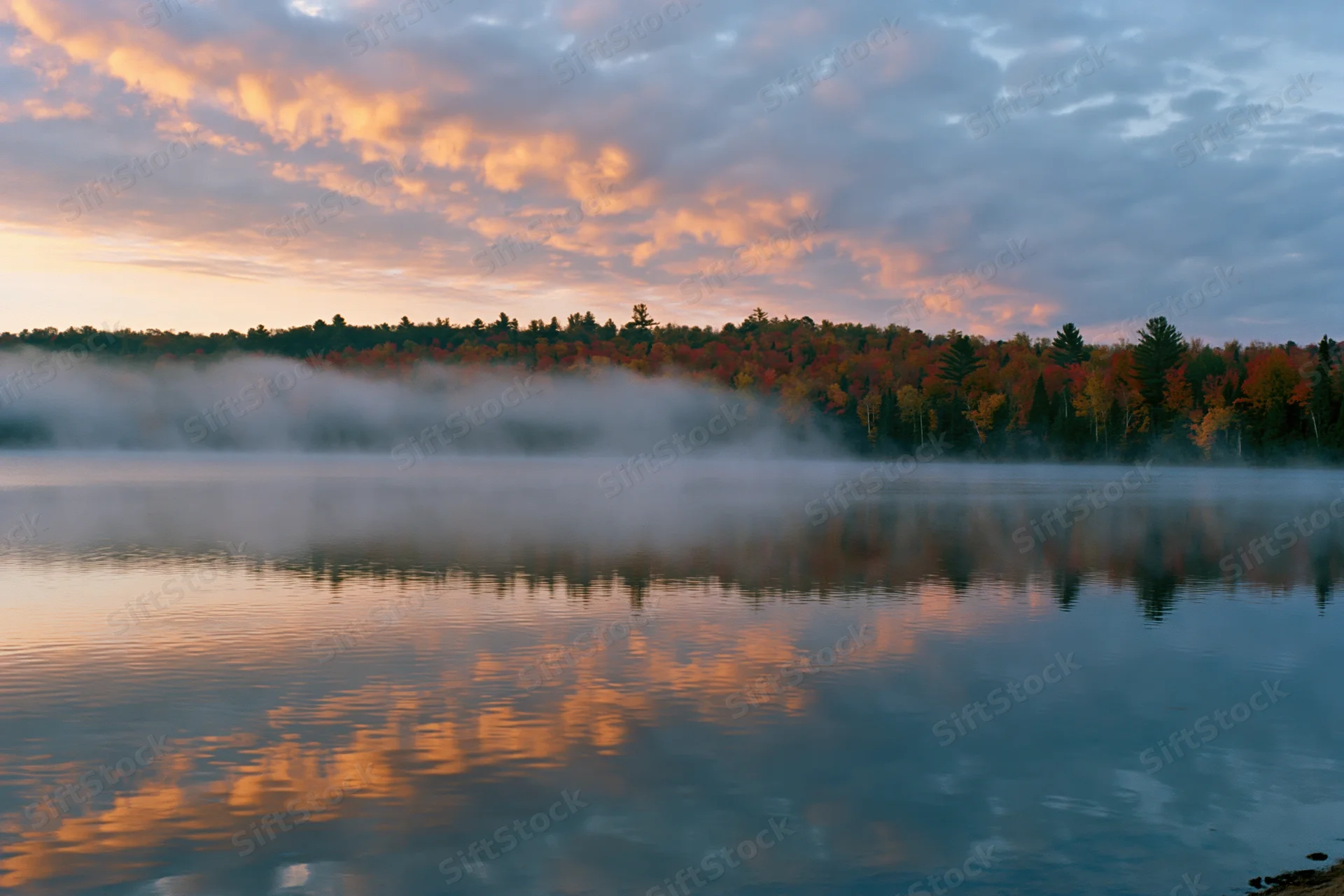Calm lake reflecting autumn trees and misty sky at dawn