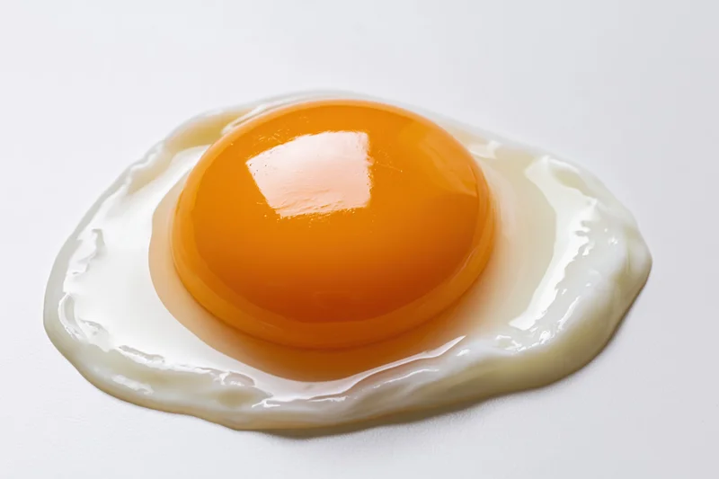 Raw cracked egg with intact yolk resting on flat white surface