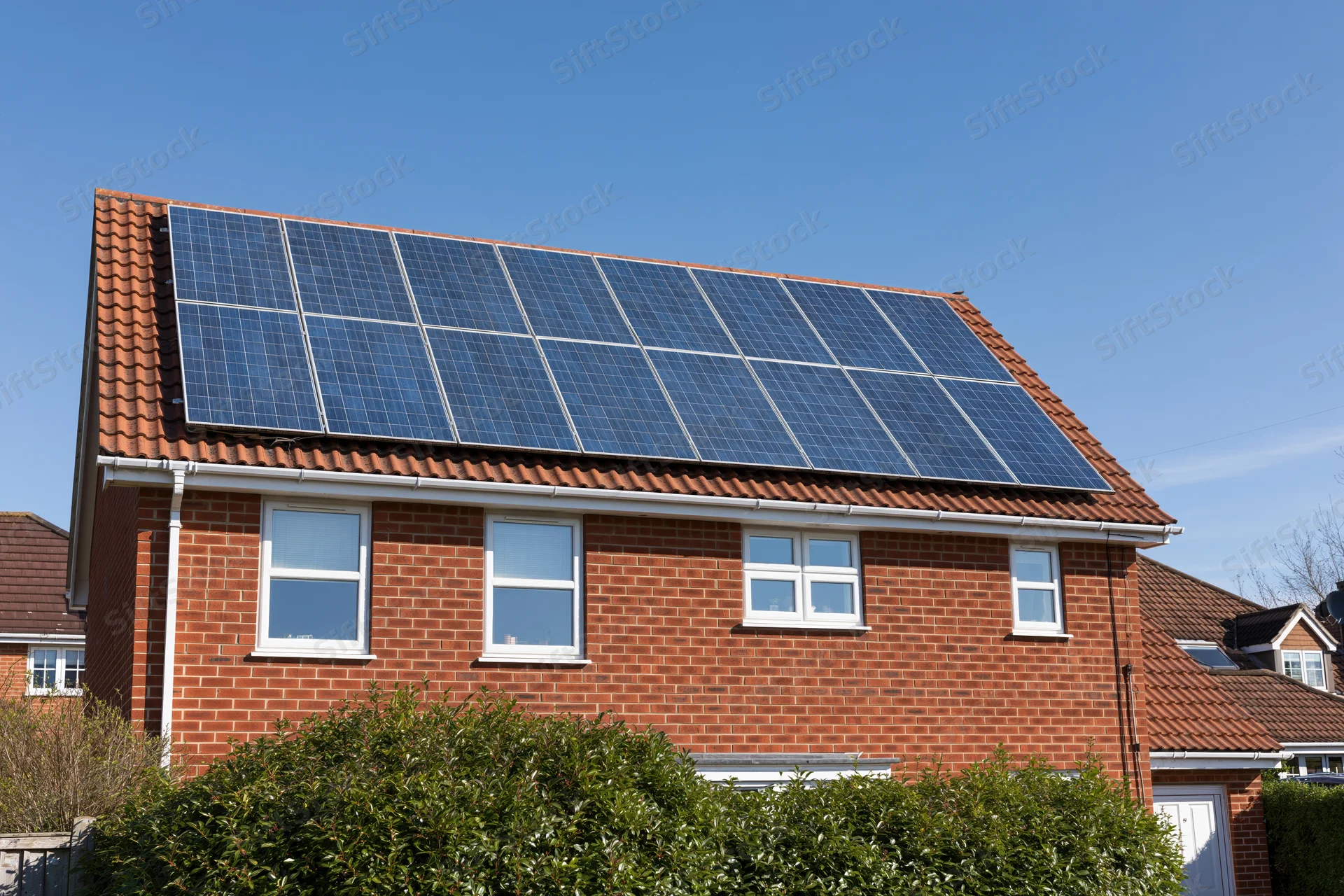 Brick residential house with solar panels mounted on the roof in a suburban neighborhood