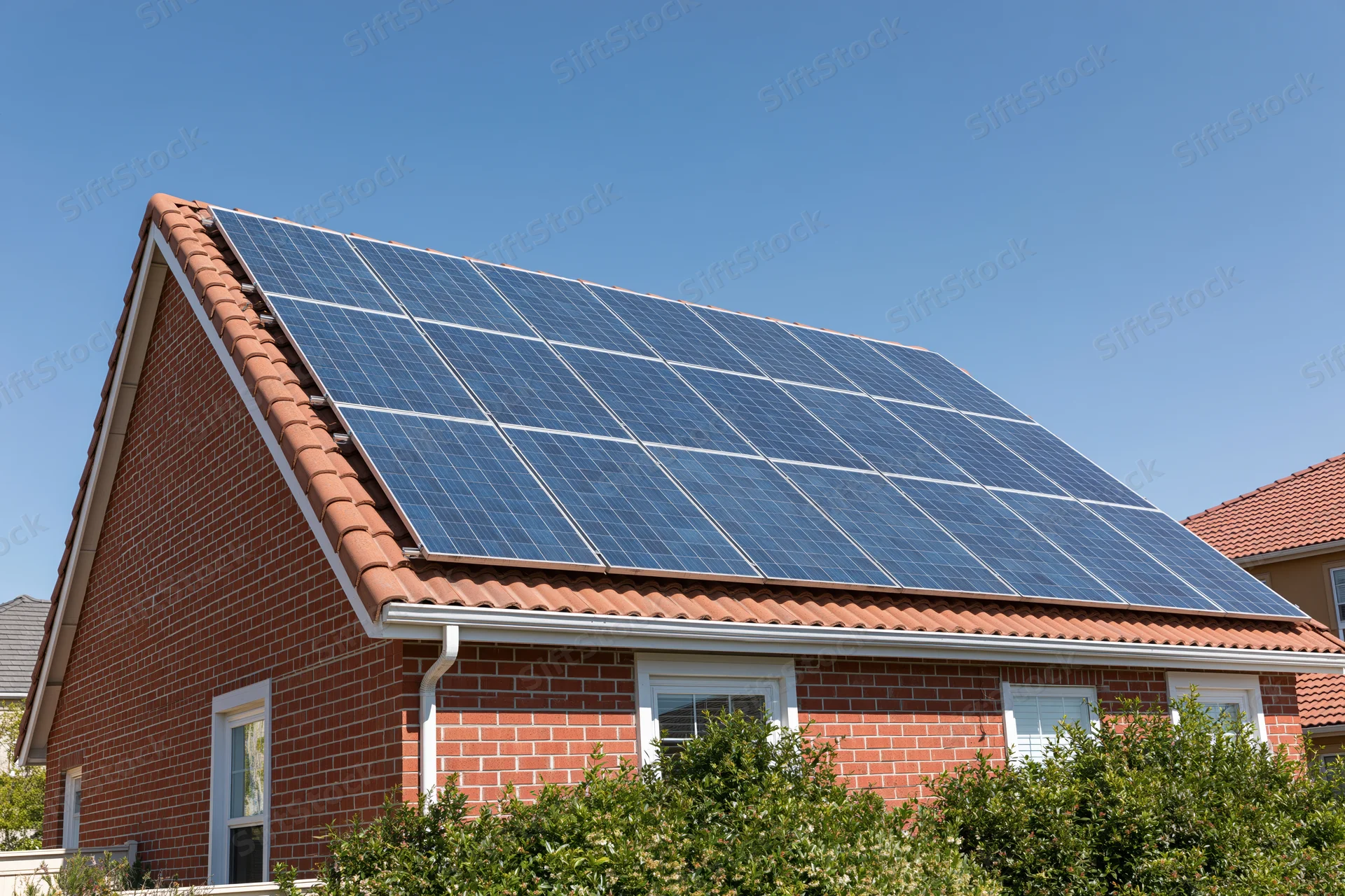 Residential brick house with solar panels mounted on the roof under clear blue sky
