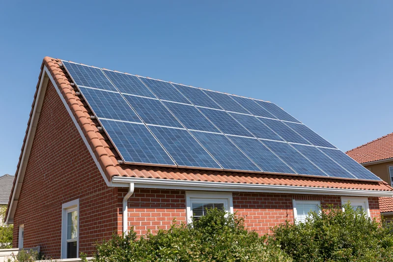 Residential brick house with solar panels mounted on the roof under clear blue sky