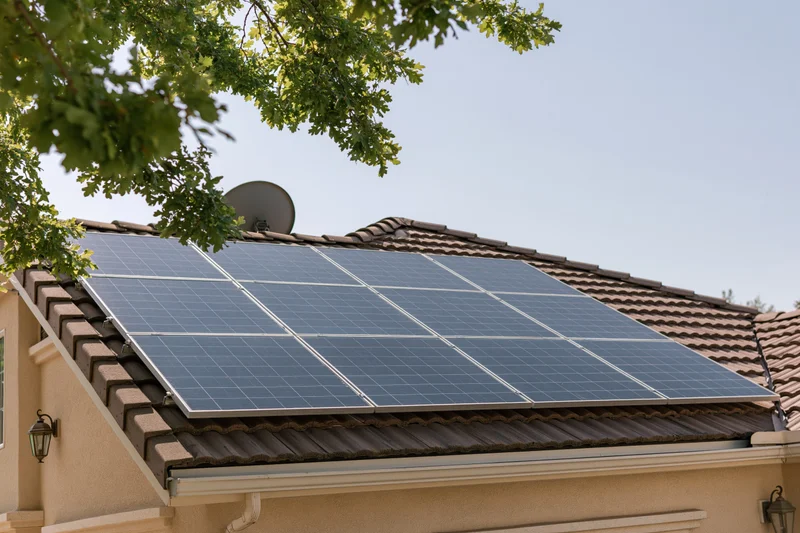 Solar panels installed on a residential rooftop with brown shingles and a satellite dish nearby