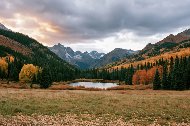 Alpine lake surrounded by autumn-colored trees and mountains in a valley meadow