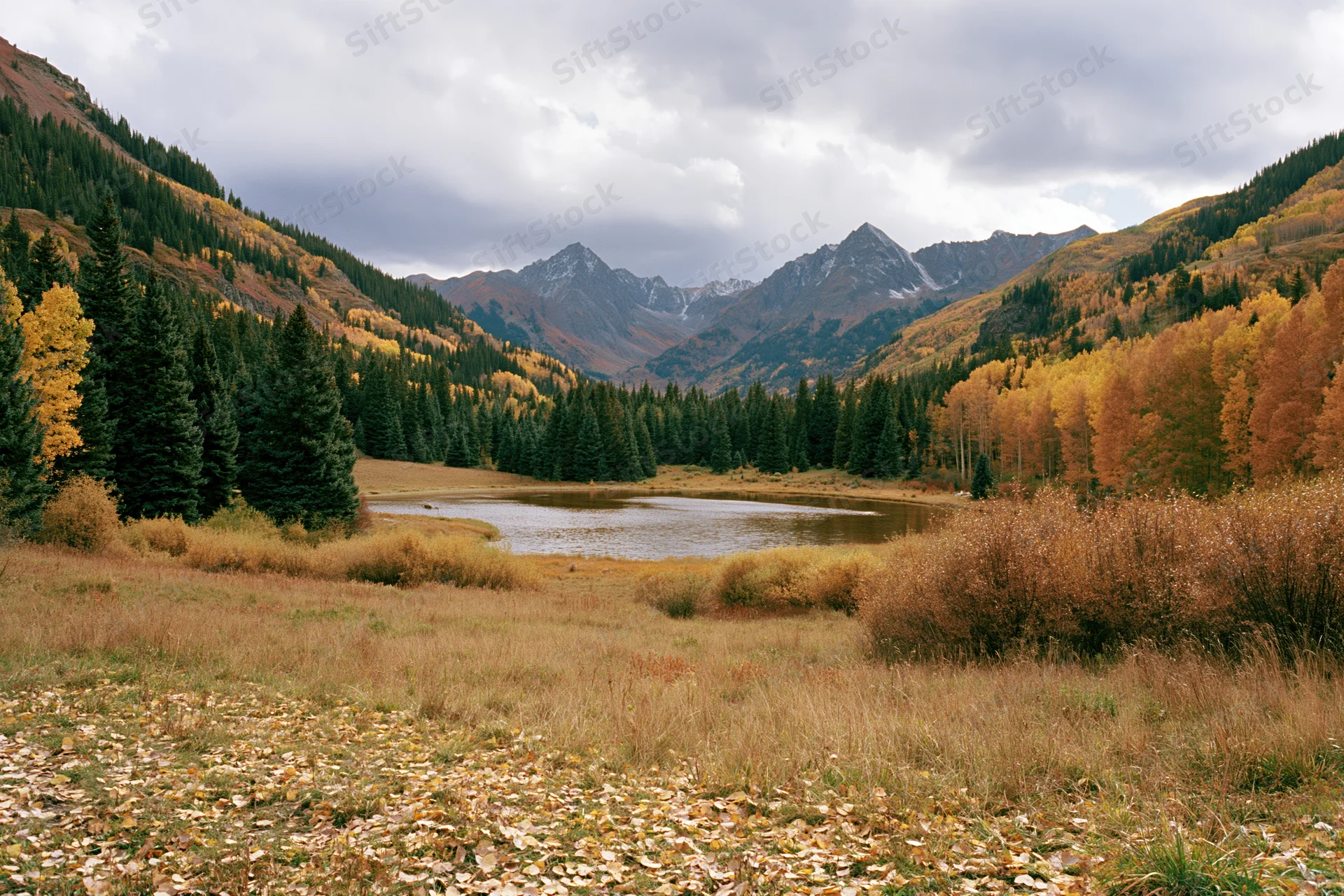 Alpine lake surrounded by autumn-colored aspen and evergreen trees in a mountain valley