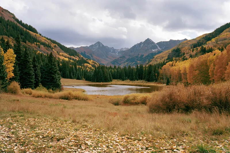 Alpine lake surrounded by autumn-colored aspen and evergreen trees in a mountain valley