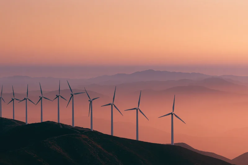 Row of wind turbines silhouetted on a mountain ridgeline at sunset