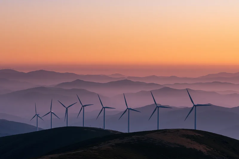 Row of wind turbines silhouetted on a mountain ridgeline at sunset