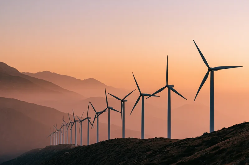 Row of wind turbines silhouetted on a mountain ridgeline at sunset