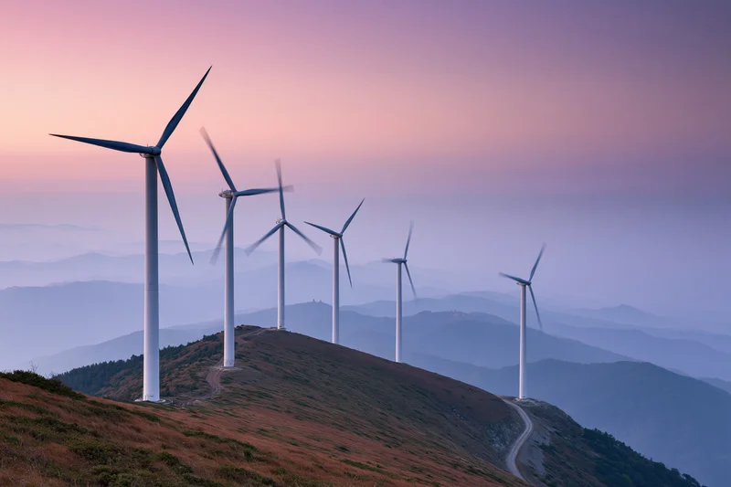 Row of wind turbines along a mountain ridge at dusk