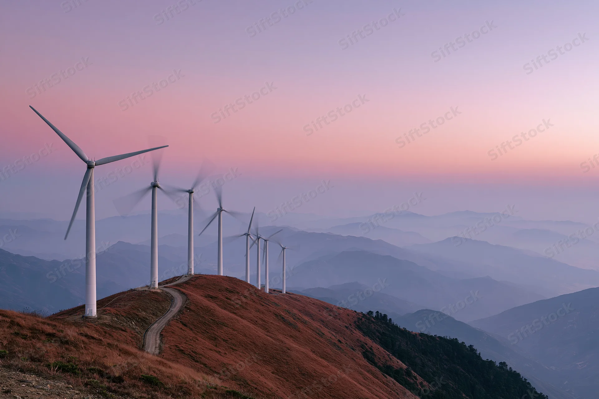 Row of wind turbines along a mountain ridge at dusk
