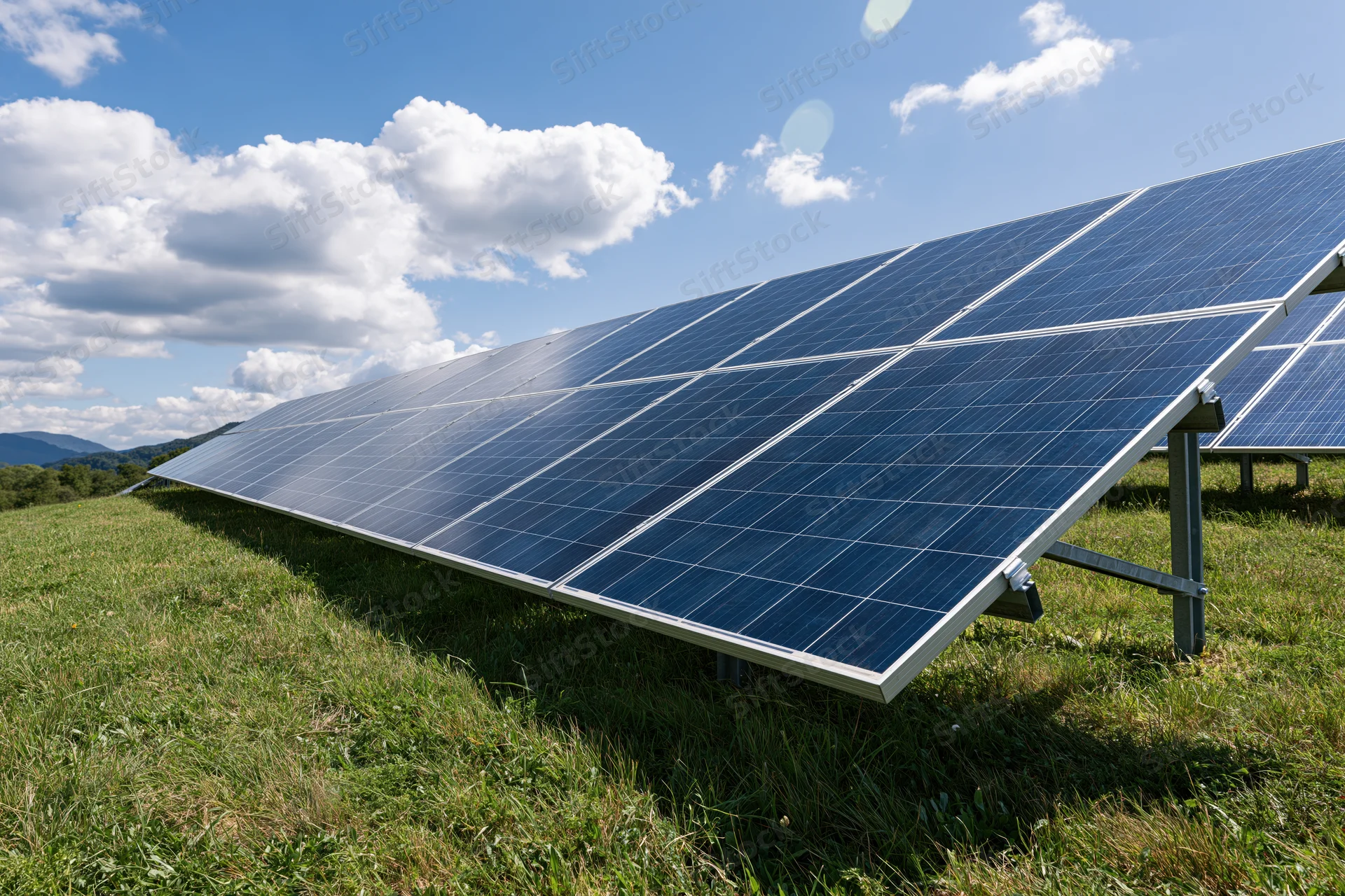 Rows of blue photovoltaic solar panels installed on a grassy field under a partly cloudy sky