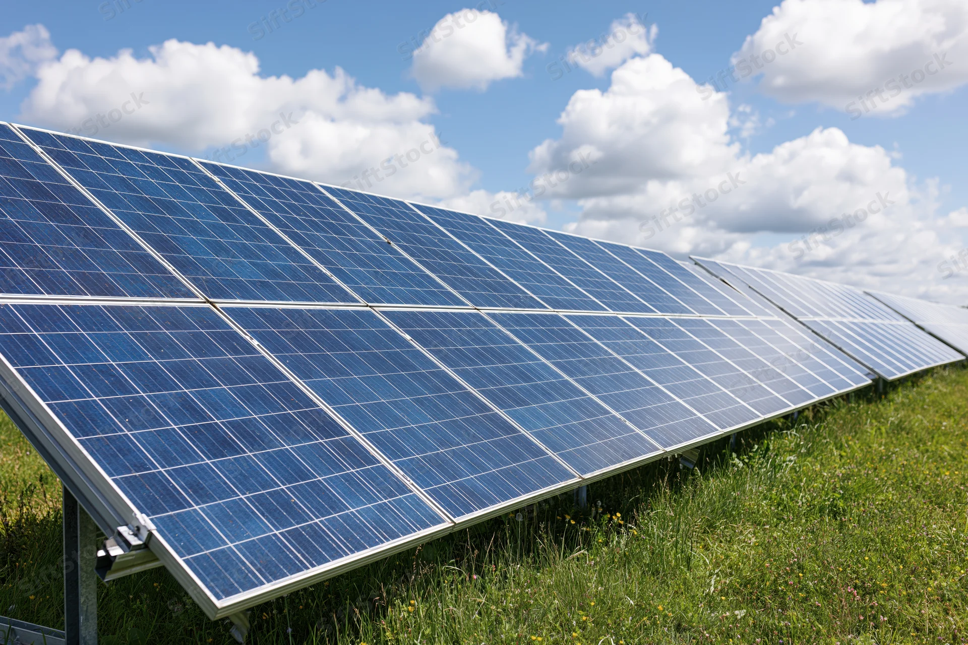 Rows of ground-mounted solar panels stretching across a green field under a partly cloudy sky