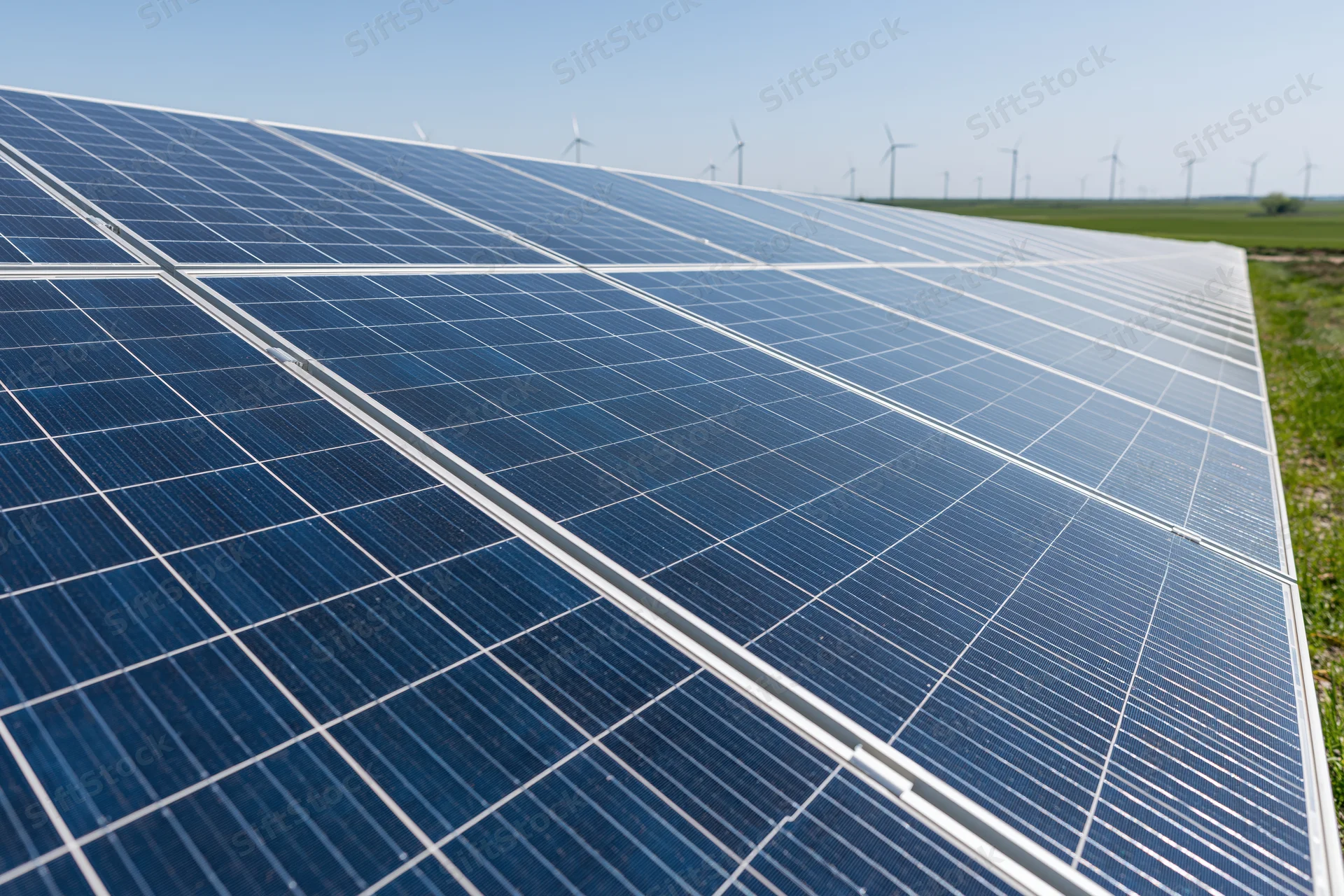 Rows of solar panels angled toward the sky in a utility-scale field with wind turbines in the distance
