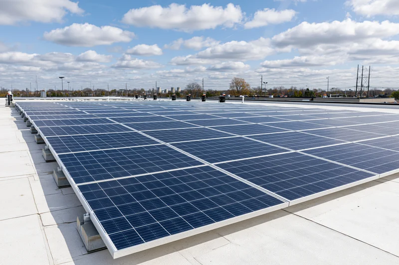 Rows of solar panels arranged in grid pattern on flat commercial rooftop under partly cloudy sky