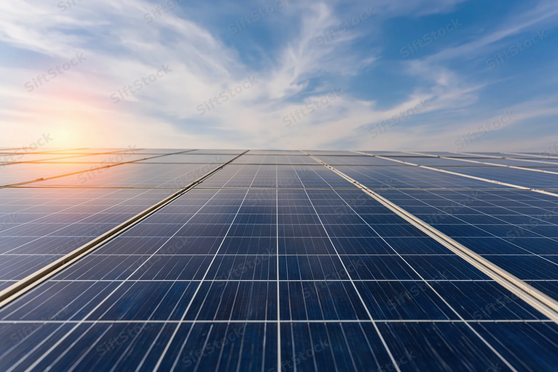 Rows of solar panels arranged in a grid under a blue sky with scattered clouds at sunrise