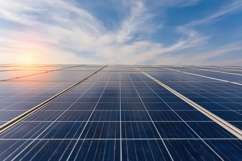 Rows of solar panels arranged in a grid under a blue sky with scattered clouds at sunrise