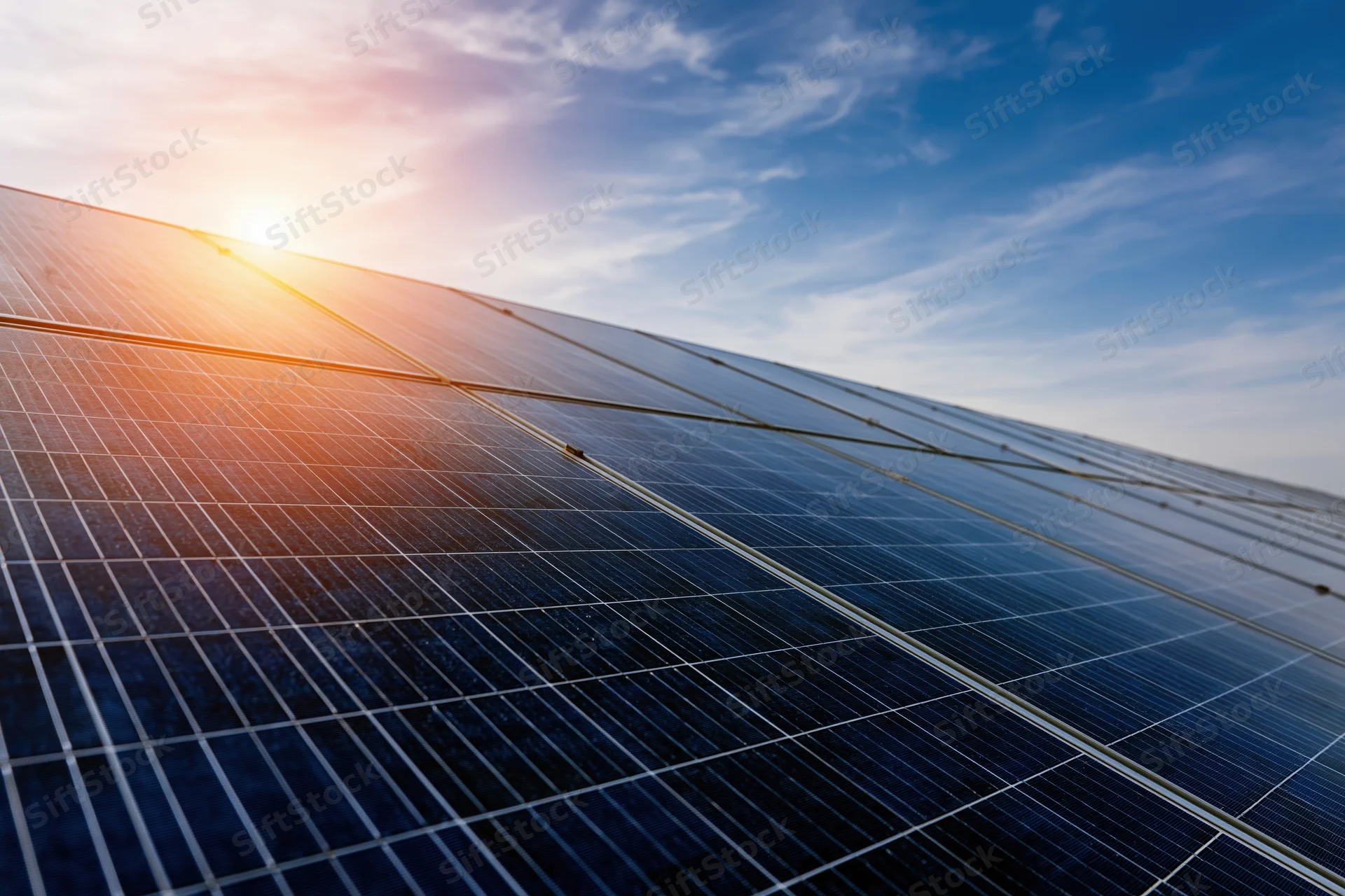 Rows of solar panels arranged in a low-angle view under a bright sky with sun flare at the horizon