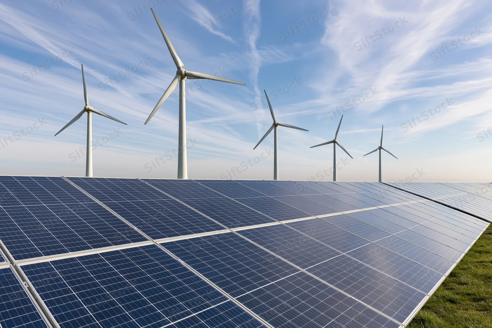 Rows of solar panels in front of wind turbines on a flat rural field under a blue sky