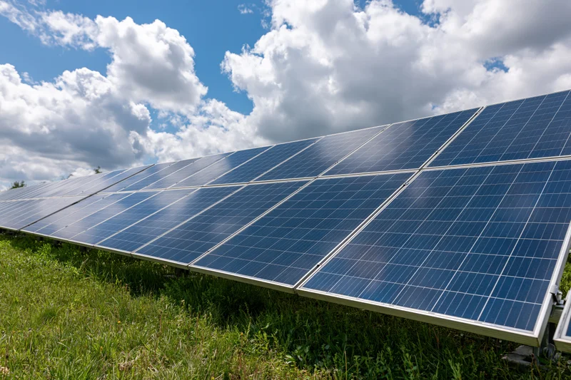 Rows of solar panels installed across a green grass field under a partly cloudy sky