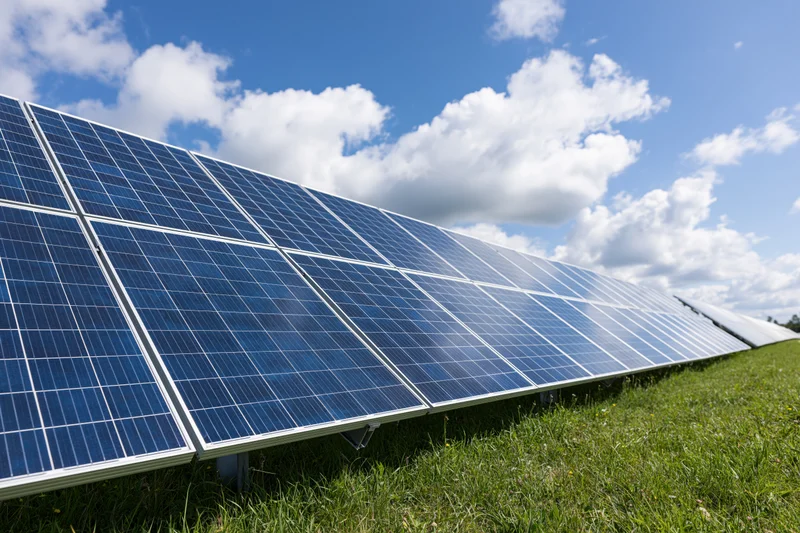 Rows of solar panels installed across a green grass field under a blue sky with white clouds