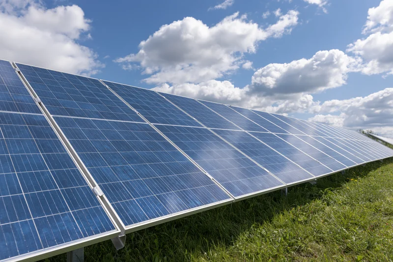 Rows of solar panels installed across a green grass field under a blue sky with white clouds
